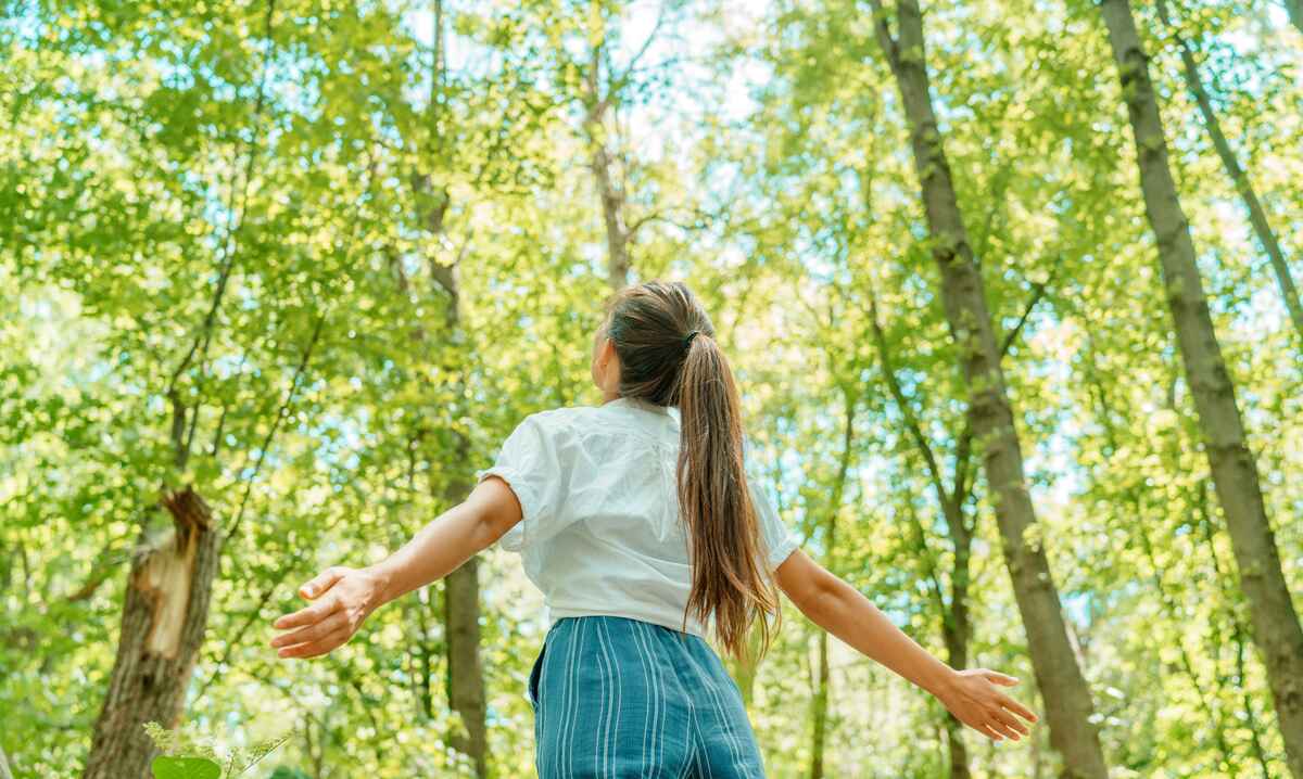 Freie Frau atmet saubere Luft in der Natur Wald. Glückliches Mädchen von hinten mit offenen Armen im Glück. Frische Outdoor-Wälder, Wellness gesunden Lebensstil Konzept